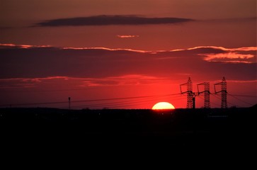 sunset through voltage poles on the hill