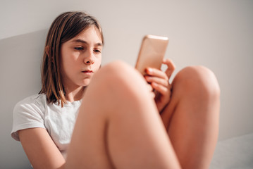 Girl sitting on the bed and using smart phone in the morning