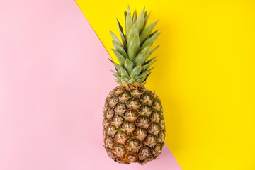 Large ripe fruit pineapple on a bright yellow and pink background. summer. top view.