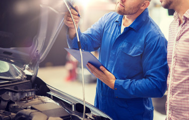 auto service, repair, maintenance and people concept - mechanic with clipboard and man or owner looking at broken car at shop