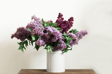 Fototapeta premium Purple bouquet of lilac flowers in a stylish vase on wooden table