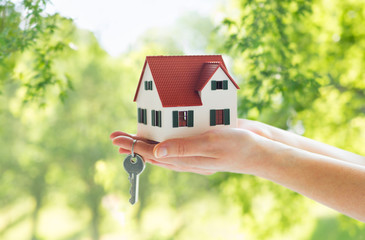 mortgage, real estate and property concept - close up of hands holding house model and home keys...