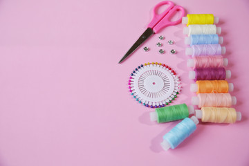 Multicolored threads of the coil, pink scissors, needle pins and buttons on a pink background. Sewing supplies, patterns and accessories for needlework, sewing, embroidery. space for text. Top view..
