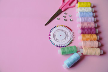 Multicolored threads of the coil, pink scissors, needle pins and buttons on a pink background. Sewing supplies, patterns and accessories for needlework, sewing, embroidery. space for text. Top view.