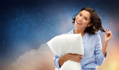 people and bedtime concept - happy young woman in pajama hugging pillow over starry night sky and cloud background