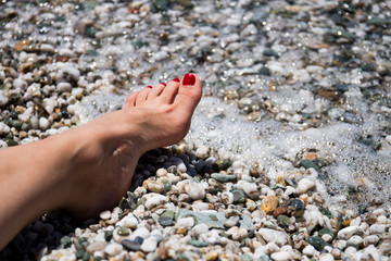 Pie de mujer dentro del agua de la playa con guijarros