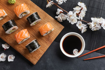 Obraz na płótnie Canvas Set of sushi and maki rolls with branch of white flowers on stone table