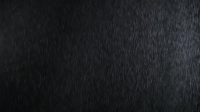 4k Heavy angled rain falling in front of the camera against black screen. Raindrops splashing. Rain closeup vfx insert. Practical seamlessly loopable footage. Heavy rainstorm hitting black surface.