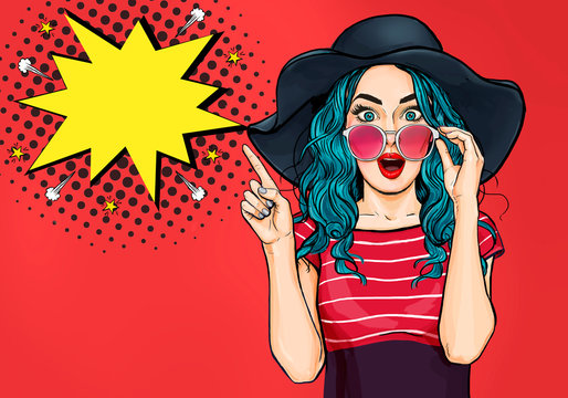 Fototapeta Pop Art Woman surprised in hat and glasses showing product .Beautiful girl with curly hair pointing to on bubble . Presenting your product. Expressive facial expressions