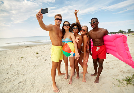 friendship, summer holidays and people concept - group of happy friends taking picture by smartphone on beach