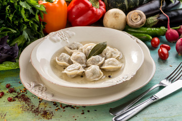 Russian meat dumplings pelmeni with bay leaf and fresh vegetables on blue wooden table