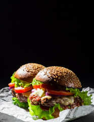two burger with meat, cheese and vegetables on dark black background