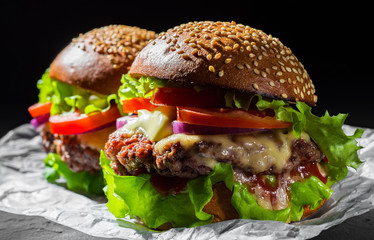 two burger with meat, cheese and vegetables on dark black background