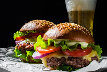 two burger with meat, cheese and vegetables and beer on dark black background