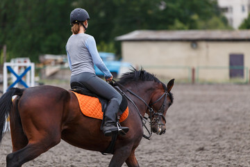 Young girl riding bay horse on equestrian sport training