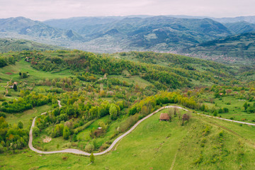 Drone view of green meadows, small houses and roads in Transylvania, Romania.