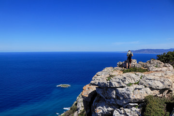 Back view of freedom man stand on rock cliff looking at blue sea and Cypriot nature. Contrast between midget and infinitely water land. Rock hill in Akamas peninsula national park with athlete