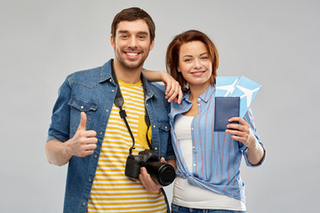 travel, tourism and vacation concept - happy couple with air tickets, passport and camera over grey background