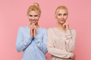 Beautiful young blonde twins conceived something interesting and do not want to disclose their secret to anyone. Look mysterious and thoughtful isolated over pink background. - obrazy, fototapety, plakaty