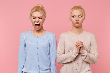 Young cute blonde woman frightened looks at her screaming sister isolated over pink background, people and emotions concept.