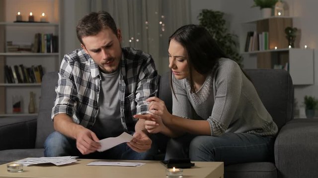Preoccupied couple accounting checking receipts sitting on a couch in the night at home