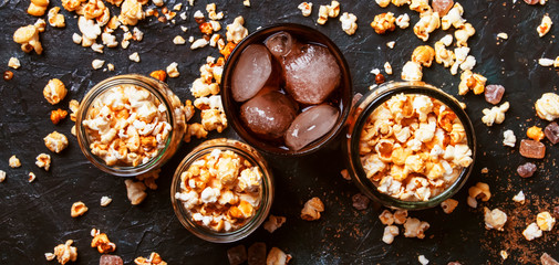 Ice cola and caramel popcorn, unhealthy food and drink, black table, top view