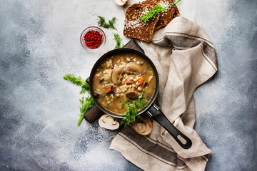 Hot meat vegetable mushroom soup with beef and wholegrain barley. With black bread, in metal pan, top view, gray kitchen table, copy space
