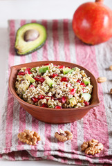 Salad of germinated buckwheat, avocado, walnut and pomegranate seeds in clay plate on white wooden background.