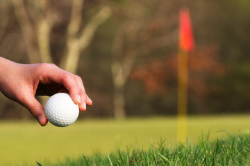 hole in green of golf course with red  flag and golfer playing