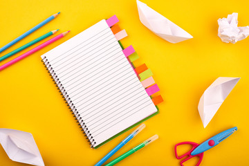 Blank white notepad with papers, pencils and scissors on yellow background