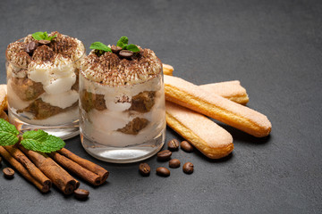Classic tiramisu dessert in a glass and savoiardi cookies on dark concrete background
