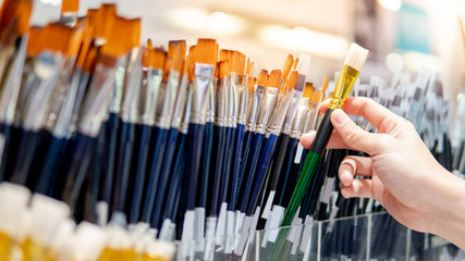 Male artist hand choosing artistic paintbrushes. New paint brushes on shelf display in stationery...