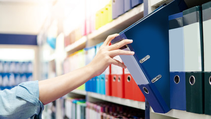 Male hand choosing new blue ring binder file folder from colorful shelf display in stationery shop....