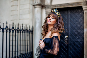 Beautiful princess in lush black dress and diadem in ancient city of Lviv