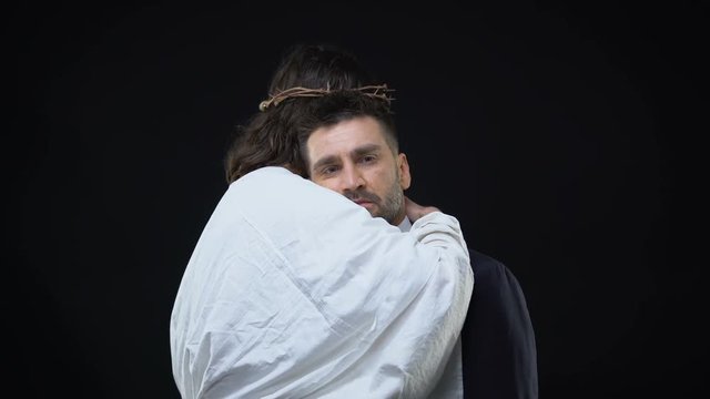 Messiah in crown of thorns hugging crying male on dark background, support