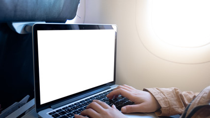Close up of young woman sitting at airplane and using laptop with blank screen and open laptop, back view
