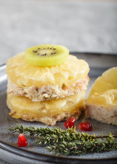 Pieces of baked pork with pineapple, cheese and kiwi on gray plate.