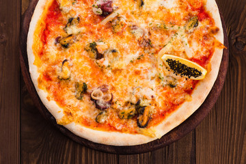 delicious Italian seafood pizza on a dark wooden table (close top view).