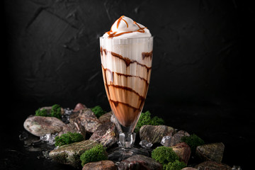 Milkshake. Cold drink of milk, ice cream, chocolate and caramel on a black background with stones and ice. Cocktail card for a bar or restaurant.
