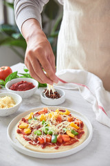 Baker's hand placing ingredients on pizza