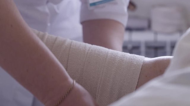 Nurse bandages a patient's leg with an elastic bandage in a hospital bed