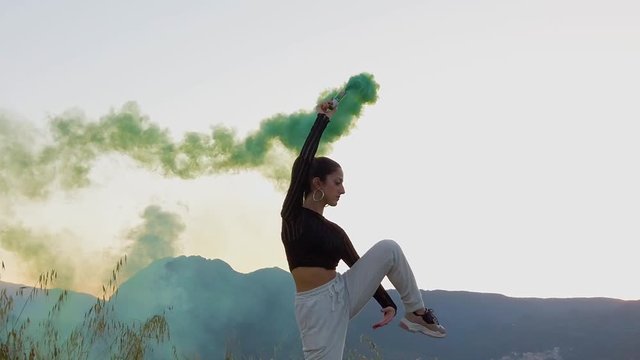 Bellissima ragazza felice, danza in una campagna con prato verde, con dei fumogeni colorati. Video al rallentatore.