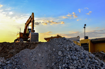 Heavy excavator bucket working in quarry on a background of sunset and blue sky. Mobile jaw stone crusher by the construction site. Crushing old concrete wastes and subsequent cement production