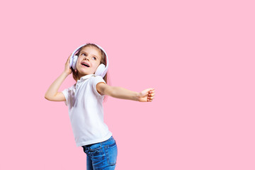 Girl listening to music in headphones on pink background. Cute child enjoying happy dance music, smile, posing on pink studio background wall.