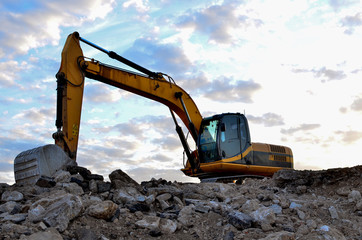 A heavy excavator in a working at granite quarry unloads old concrete stones for crushing and recycling to gravel or cement. Special heavy construction equipment for road construction.