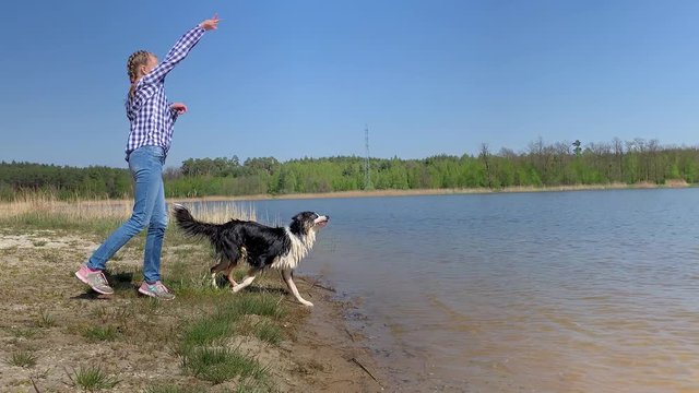 Happy teen girl play with dog on beach of river, throws her stick. Dog pulls stick out of water. Child faving fun with young Australian Shepherd dog outdoor.