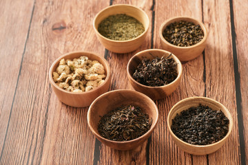 assortment of dry tea in white bowls on wooden surface