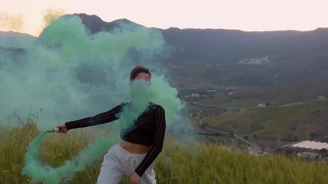 Bellissima ragazza felice, danza in una campagna con prato verde, con dei fumogeni colorati. Video al rallentatore.