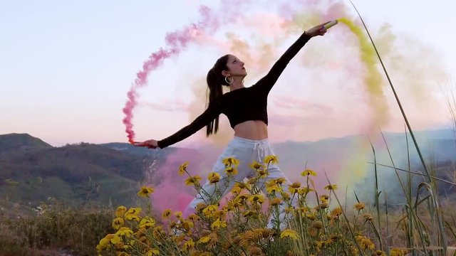 Bellissima ragazza felice, danza in una campagna con prato verde, con dei fumogeni colorati. Video al rallentatore.