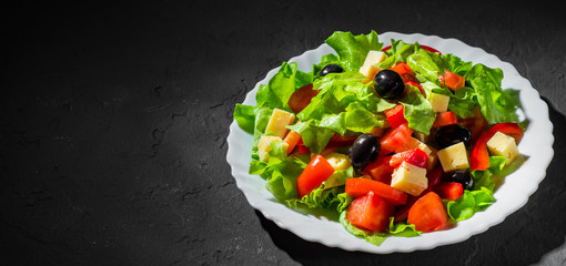 fresh vegetables salad with lettuce, olive, pepper, tomato and cheese in white plate on dark black background
